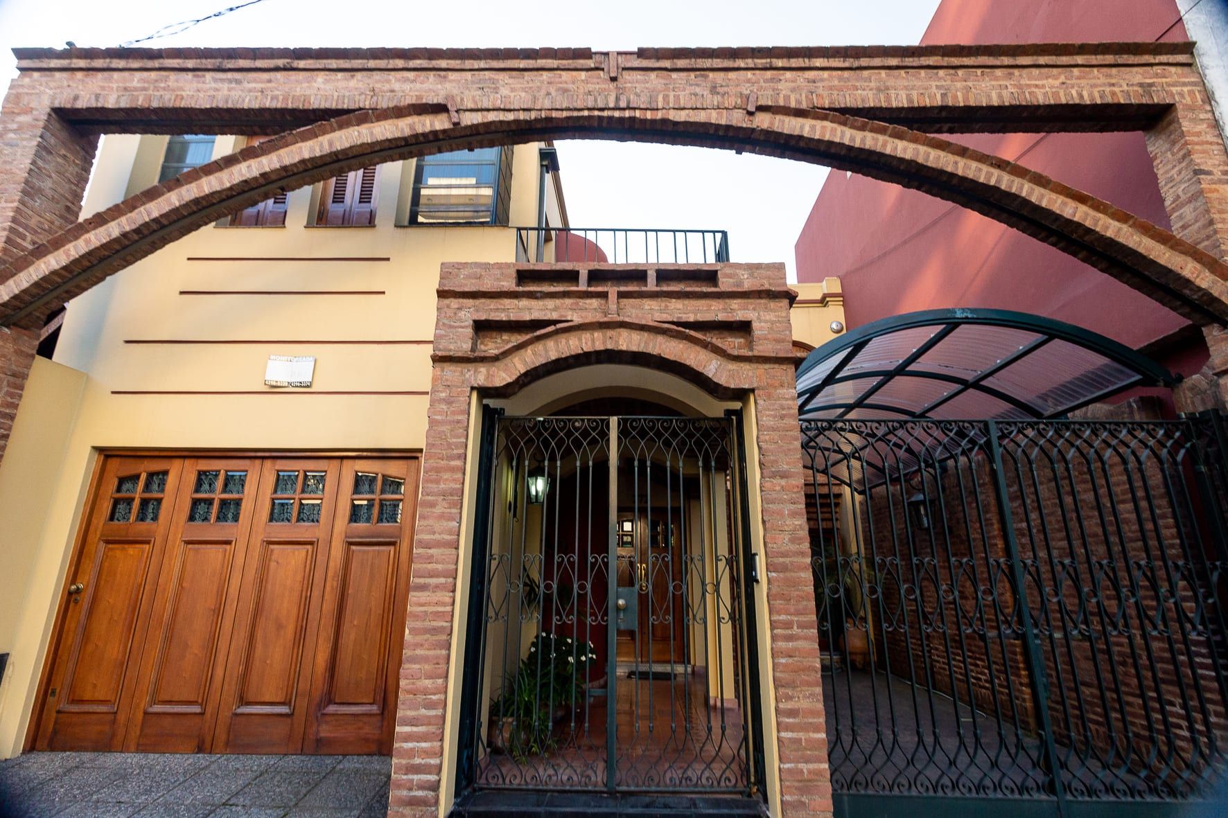 Fachada terminada de Brandsen desde la vereda: arco de ladrillo visto, portón de madera y reja de hierro forjado