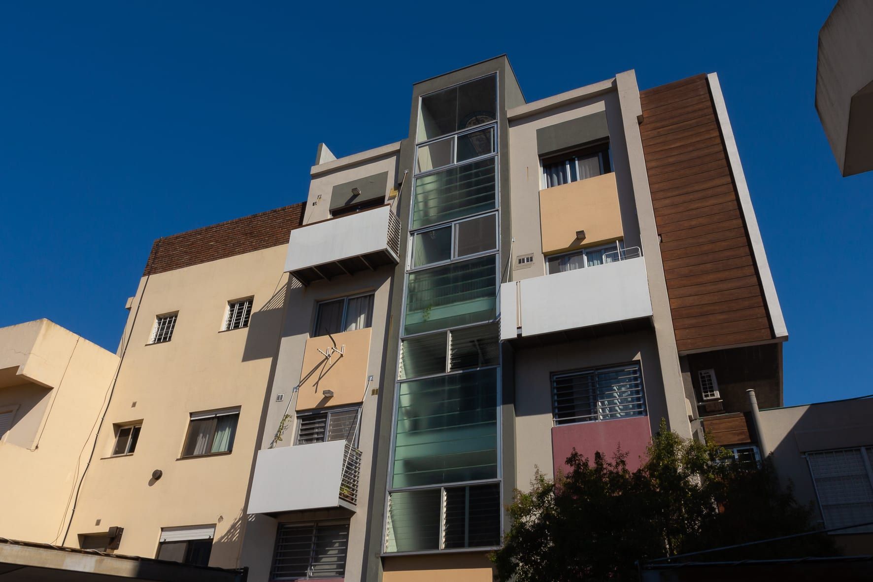 Fachada de Vicente López 404 en contrapicado: balcones blancos, paneles ocre y revestimiento de madera bajo cielo azul