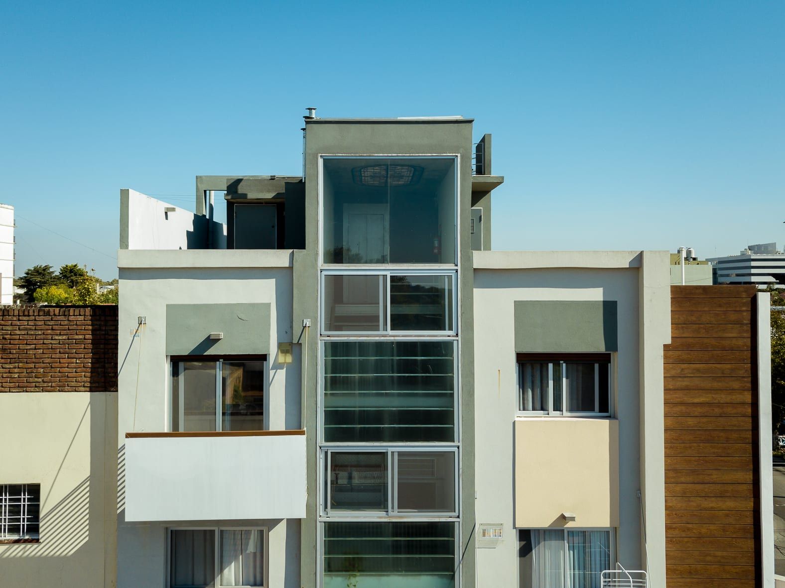 Vista frontal del edificio terminado con caja vidriada central de la escalera y terraza superior