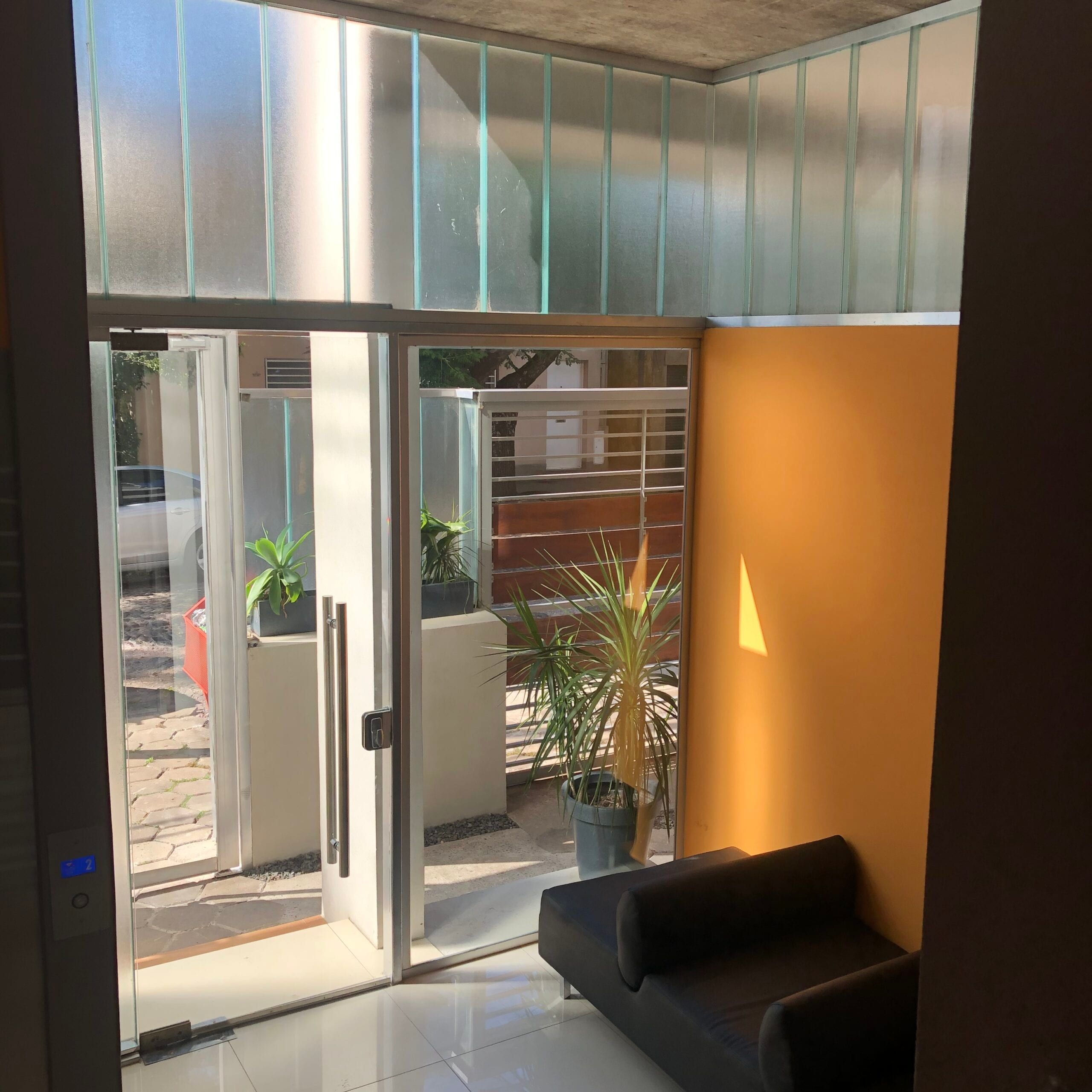 Hall de entrada de Matienzo 372 con pared naranja, sillón y cerramiento vidriado hacia la calle