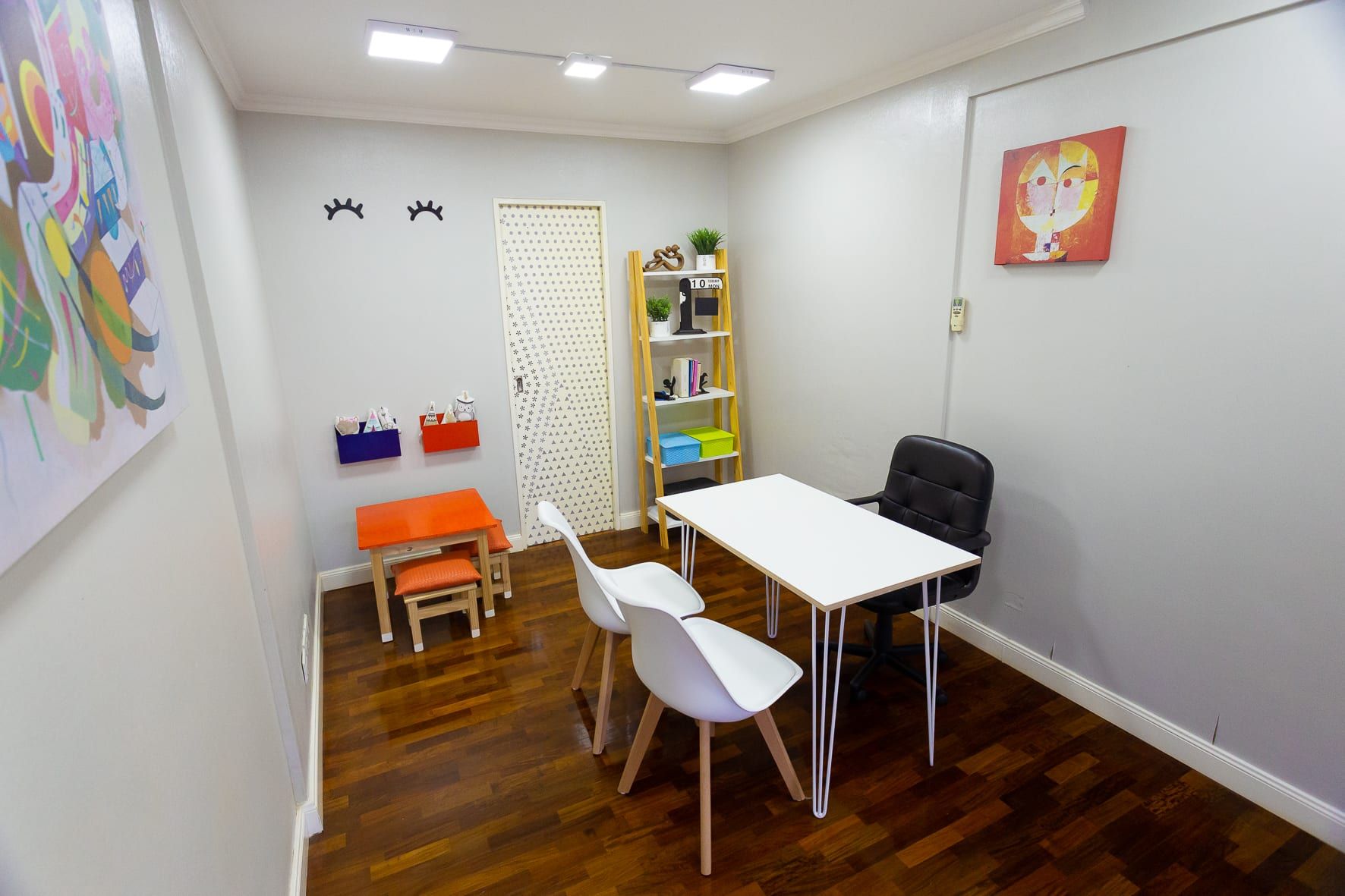 Otra vista del ambiente amueblado como consultorio, con estantería escalera, cuadros y puerta empapelada en blanco