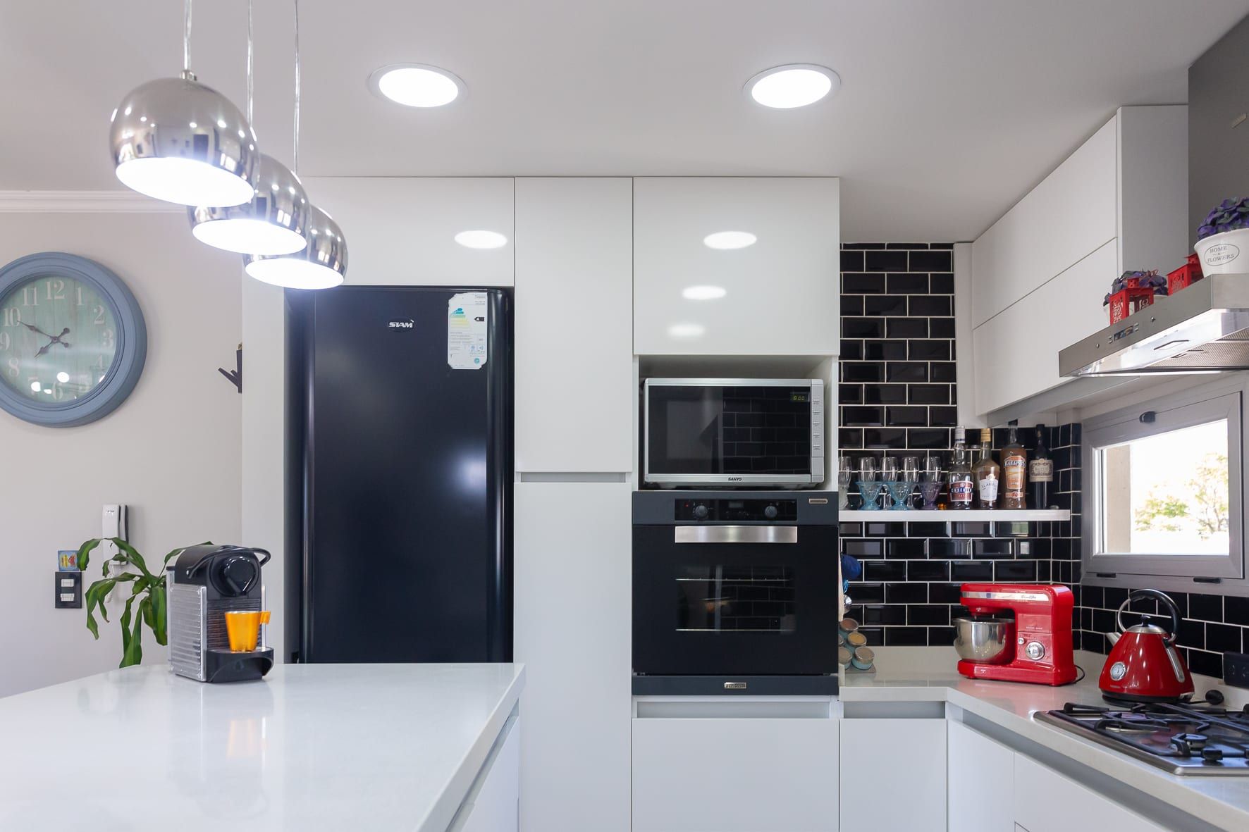 Cocina equipada con muebles blancos, horno empotrado y guarda de azulejos negros tipo subway