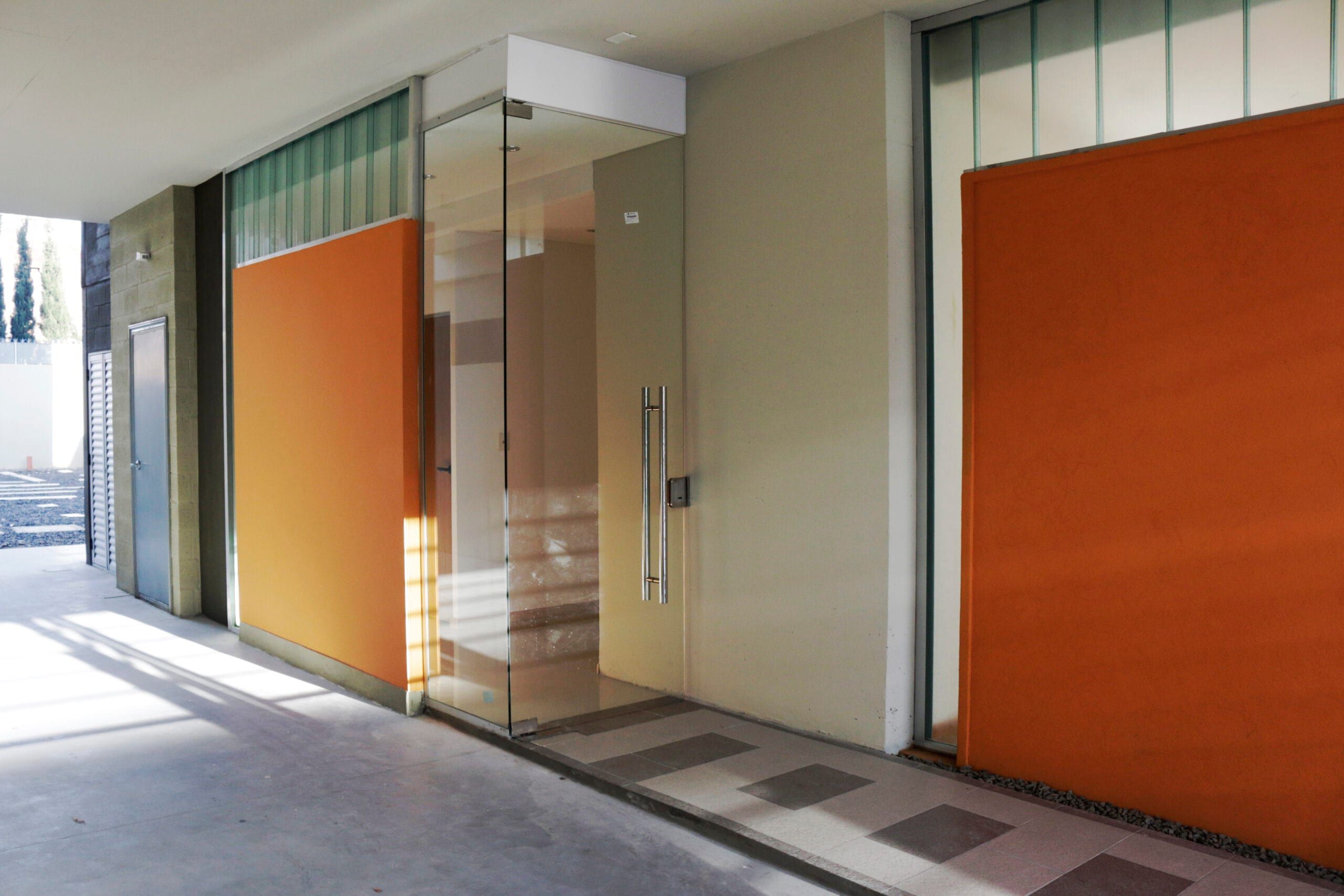 Acceso en planta baja de Yrigoyen 37: puerta de vidrio con tirador de acero entre muros naranjas