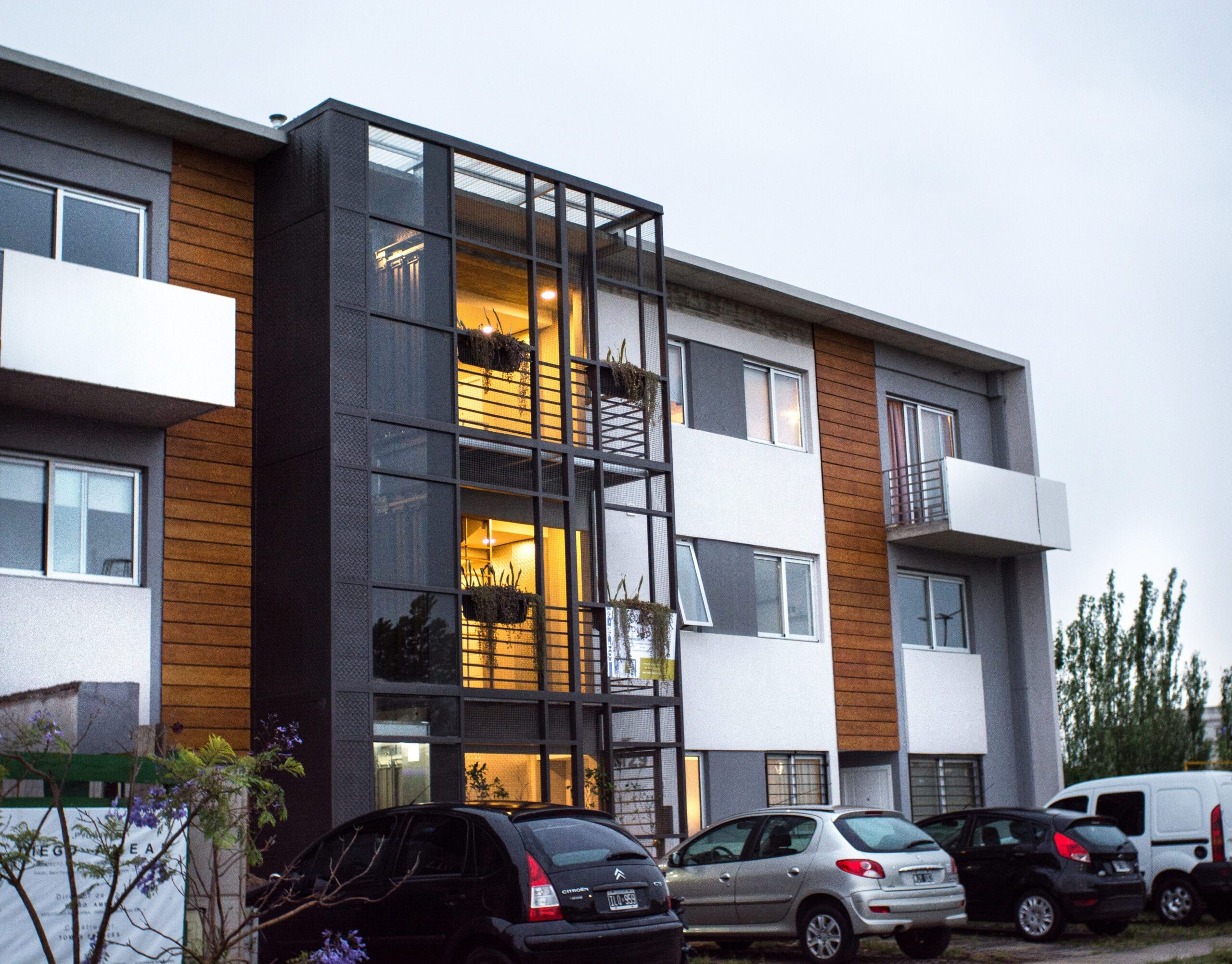 Contrafrente de Nuevo Quilmes 2M29 al atardecer con interiores iluminados, balcones y revestimiento símil madera