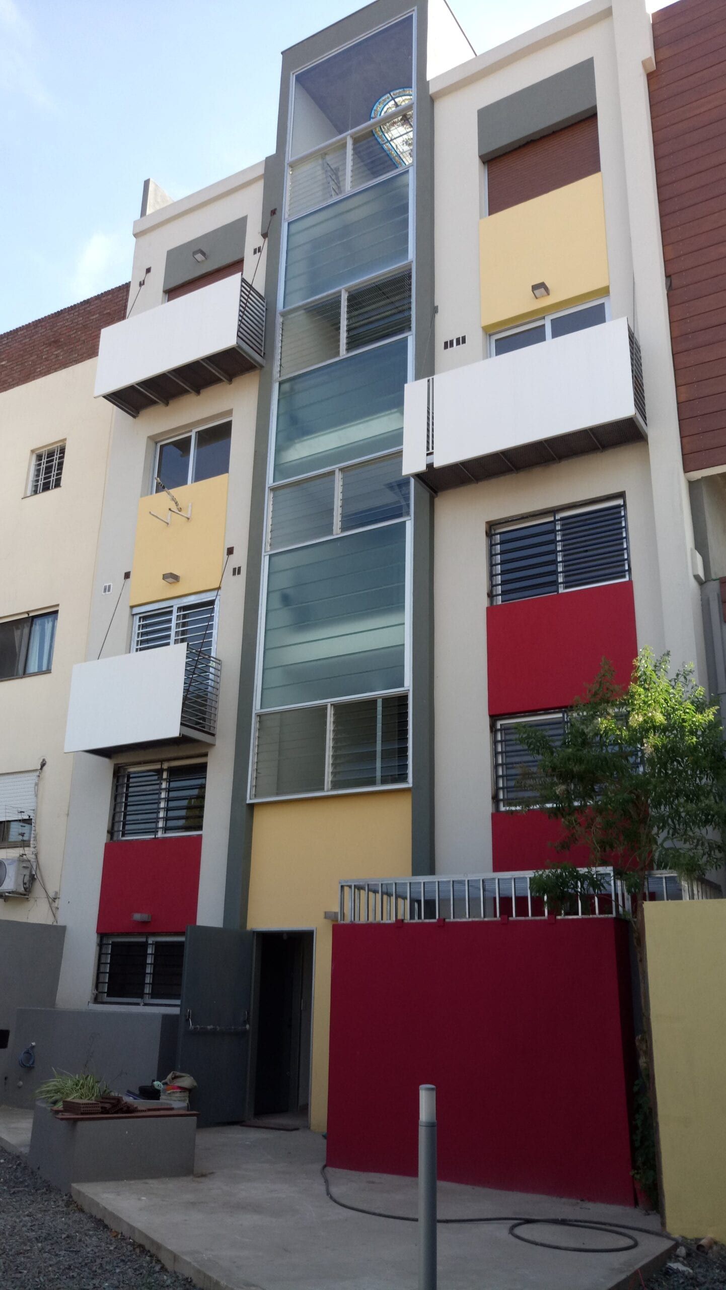 Contrafrente con patio de acceso, balcones y paneles de color rojo, amarillo y blanco sobre la caja de escalera vidriada