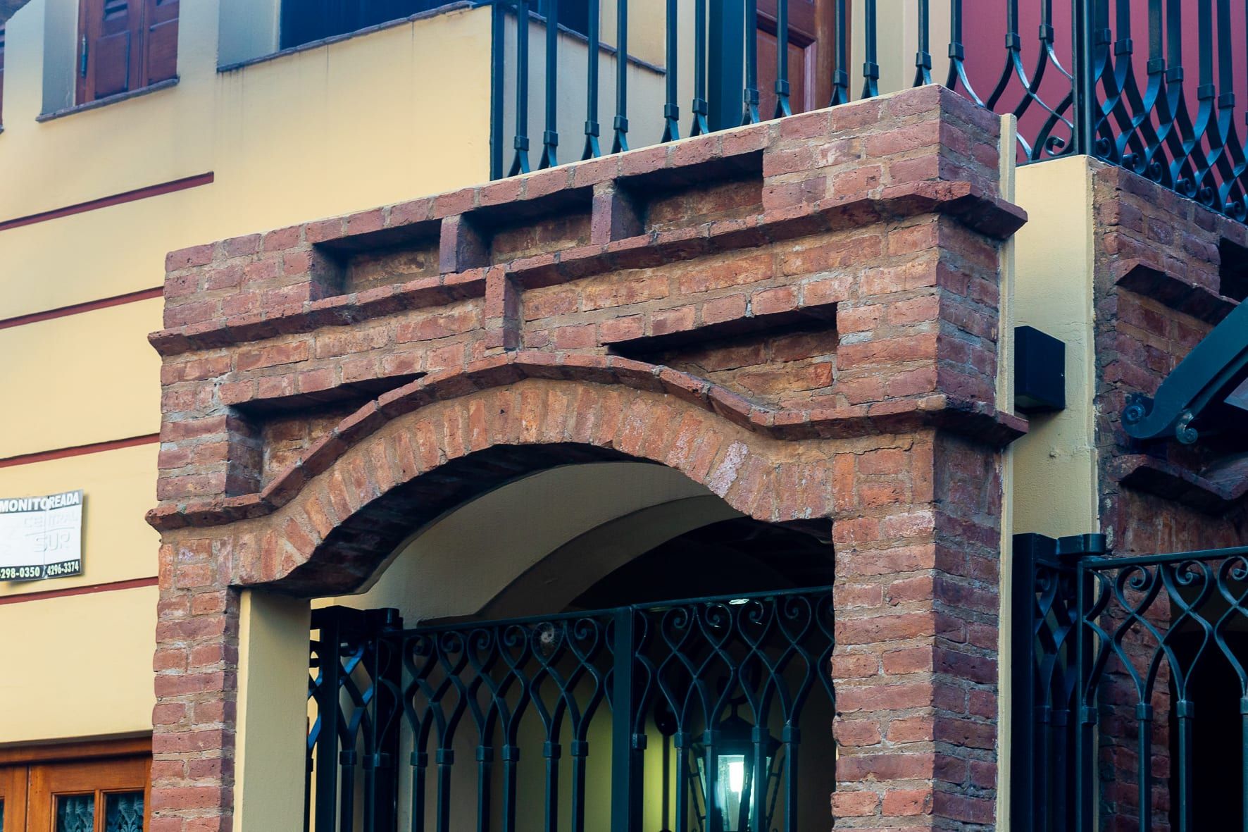 Detalle del pilar y arco de ladrillo del acceso peatonal, junto a la baranda de hierro del balcón
