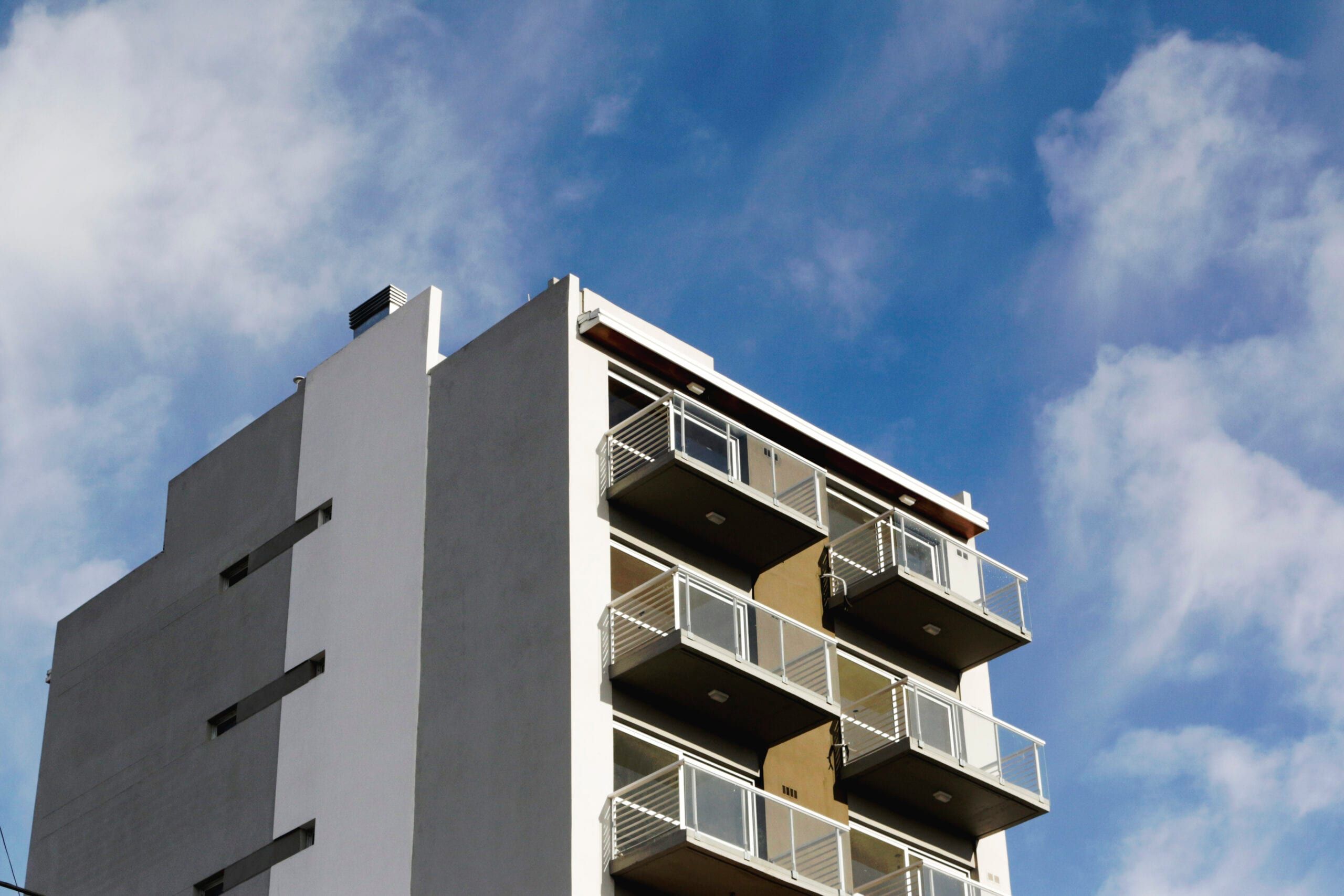 Remate superior de Yrigoyen 37 en contrapicado: balcones con barandas metálicas blancas contra cielo despejado