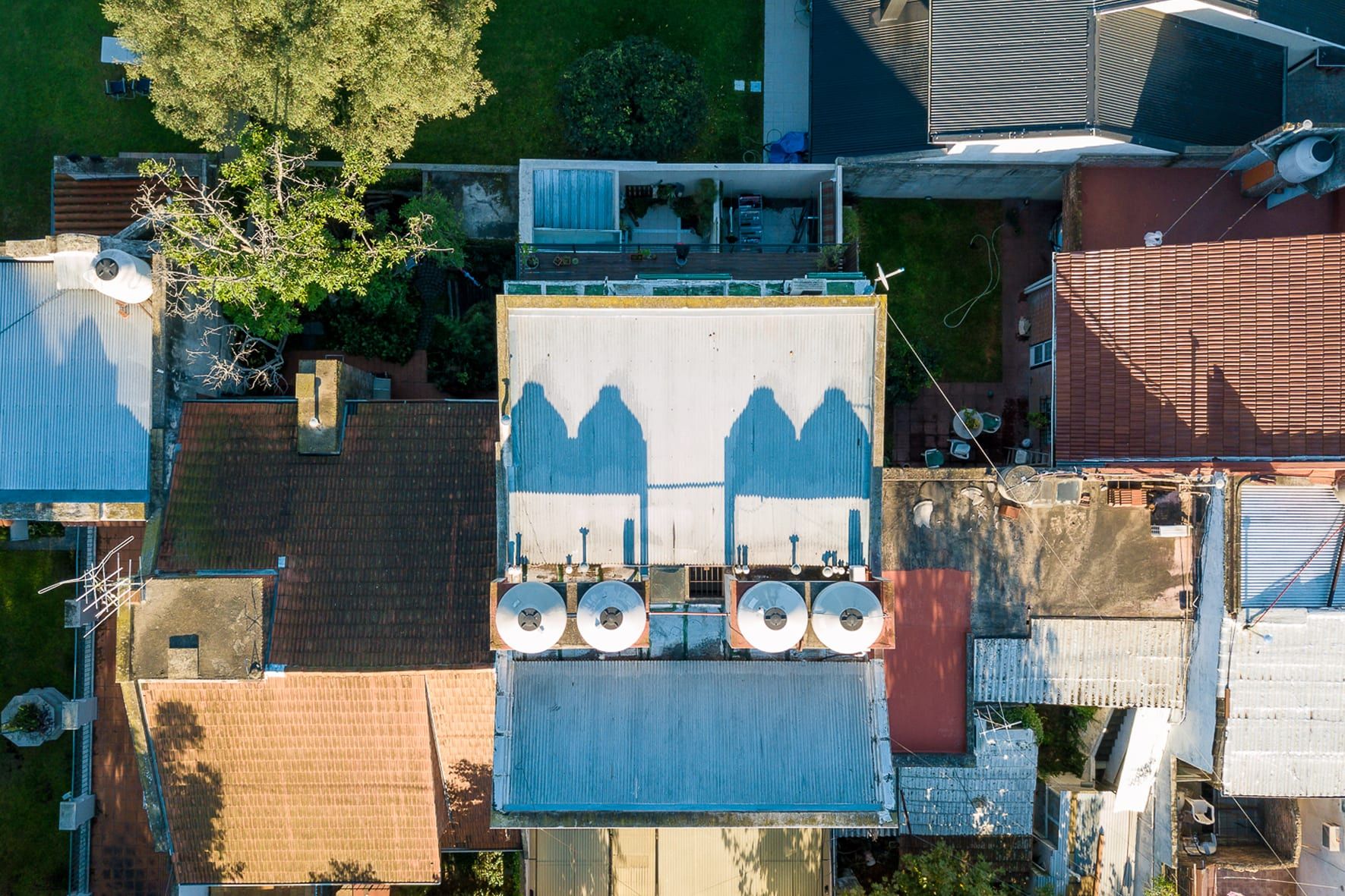 Vista cenital con dron de Rawson 140: azotea con tanques y deck en la terraza, entre techos linderos de Bernal