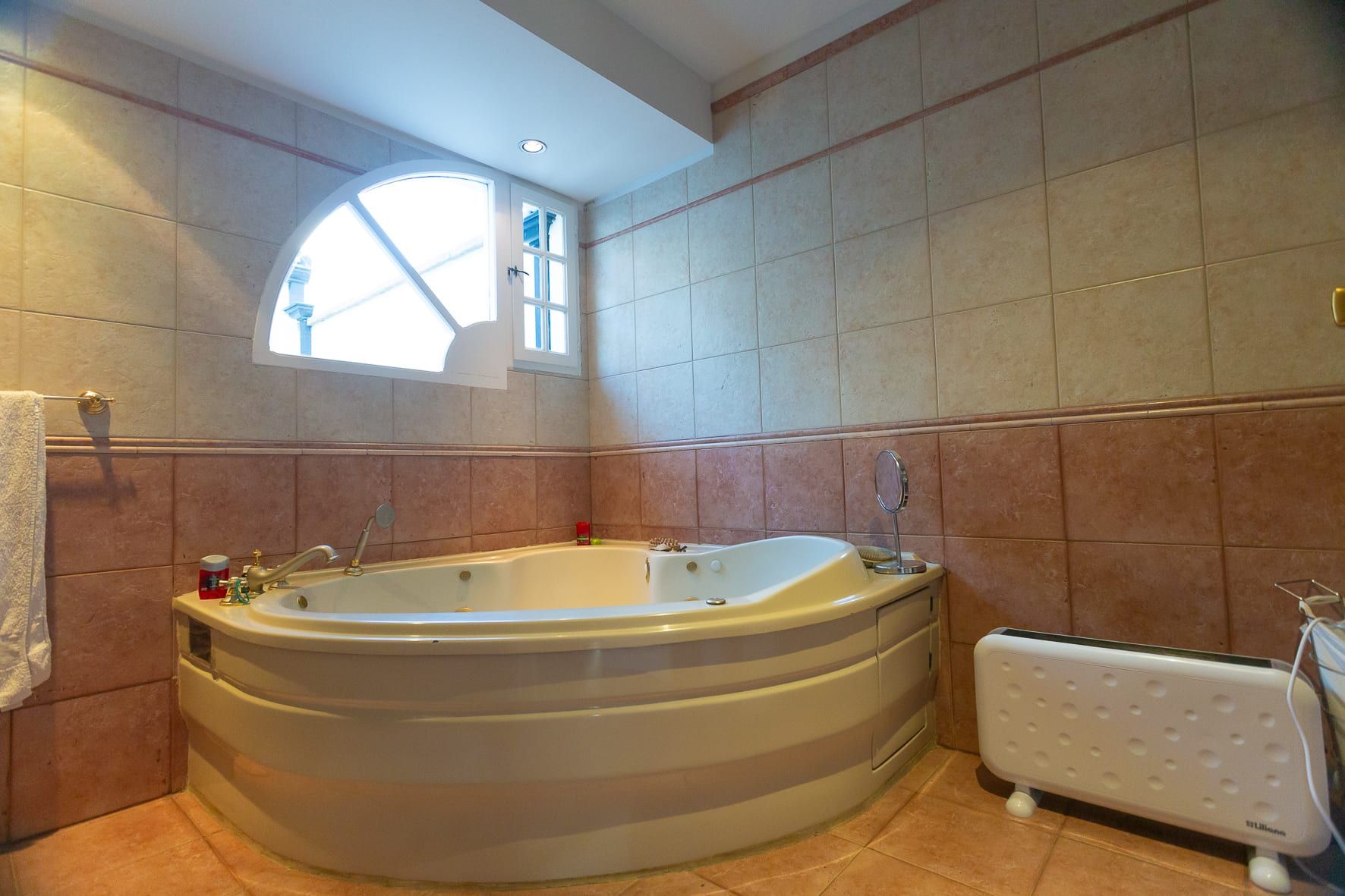 Baño principal con hidromasaje de esquina, ventana en medio punto y revestimiento cerámico