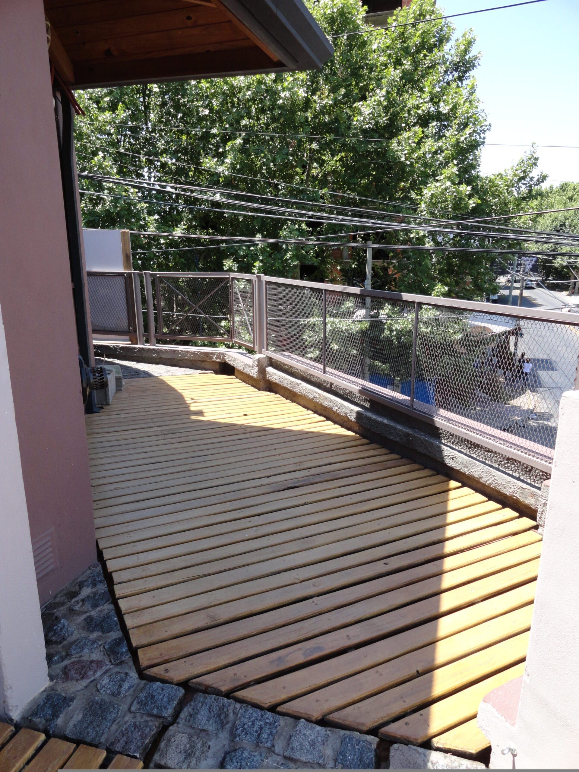 Balcón terraza con deck de madera y baranda metálica, con vista a la arboleda de la avenida en Quilmes