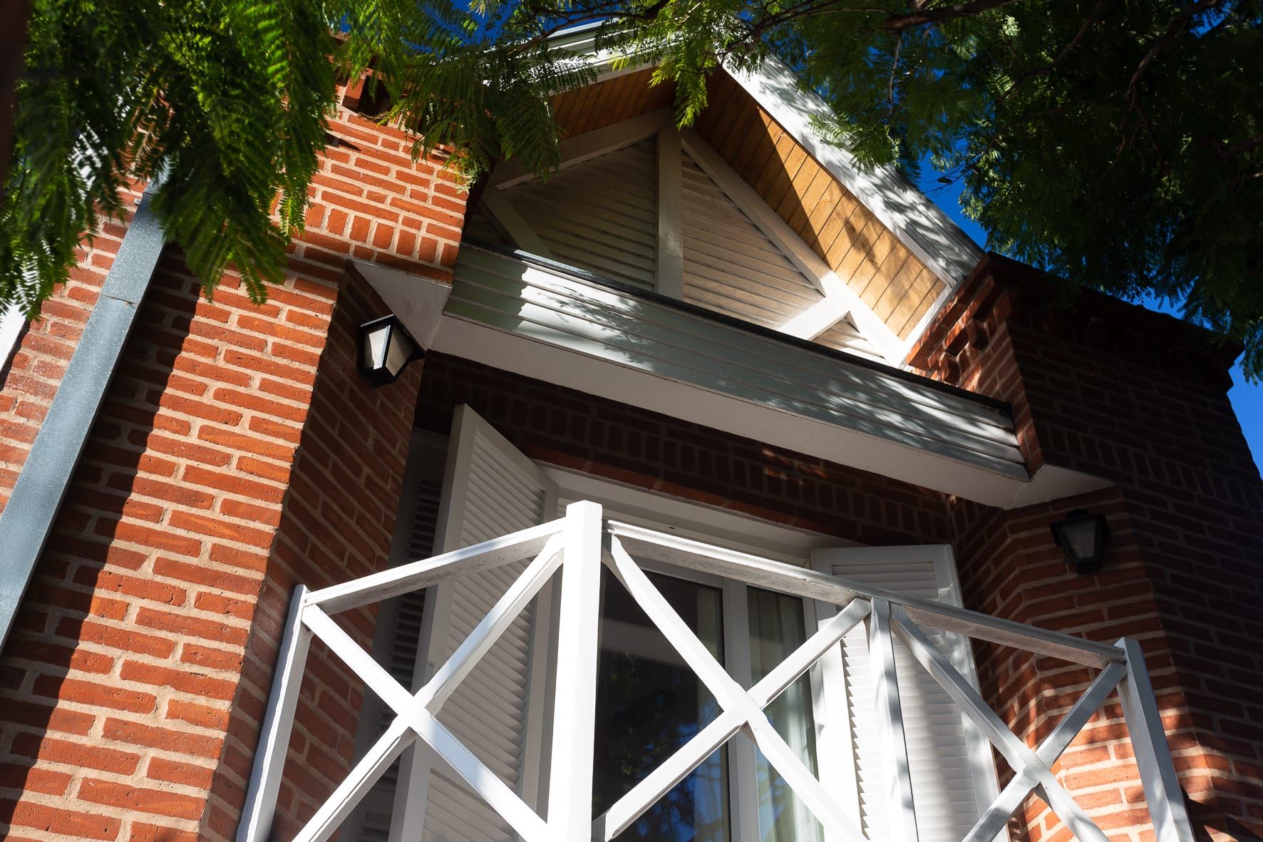 Detalle del balcón con baranda cruzada blanca y hastial de madera sobre la fachada de ladrillo